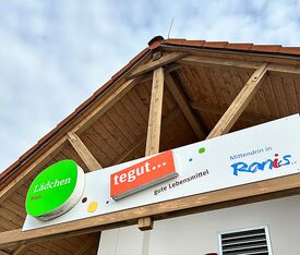 Eingangsbereich des tegut… Lädchens am Marktzentrum Ranis mit Holzgiebel und Beschilderung ‚gute Lebensmittel, Mittendrin in Ranis‘