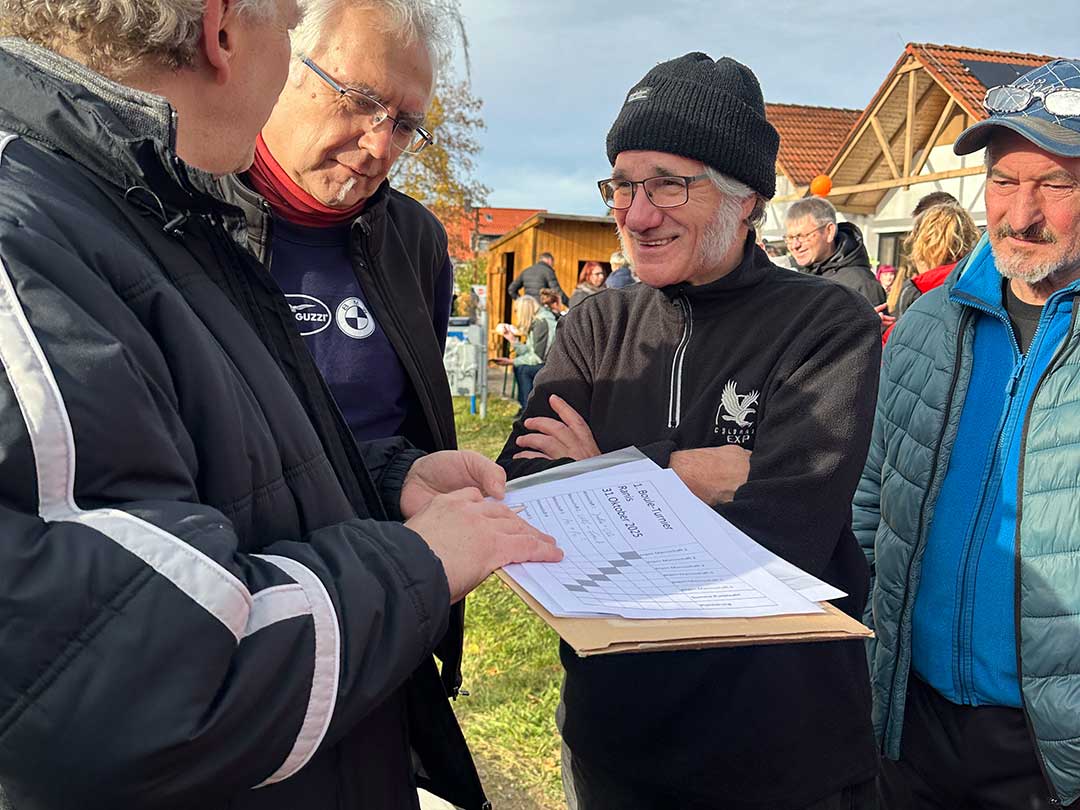 Teilnehmer des Boule-Turniers in Ranis besprechen die Spieltabelle und Ergebnisse bei sonnigem Herbstwetter vor dem Marktzentrum Ranis.