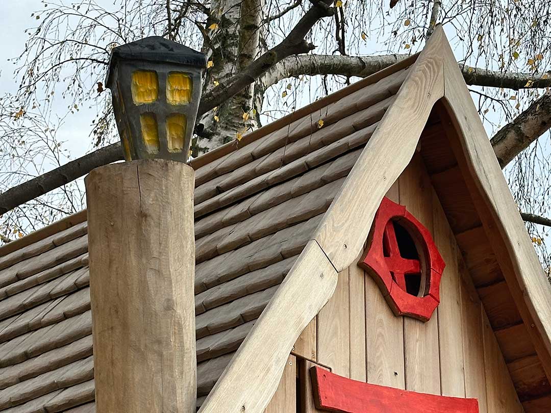 Detailansicht des hölzernen Hexenhauses mit rotem Fensterrahmen und Laterne im Spielbereich am Marktzentrum Ranis.“