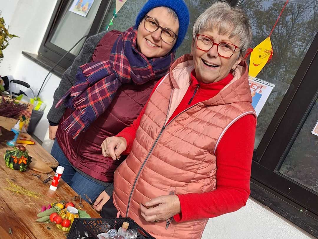 Zwei Frauen basteln herbstliche Dekorationen beim Kürbisfest am Marktzentrum Ranis und lächeln in die Kamera.“